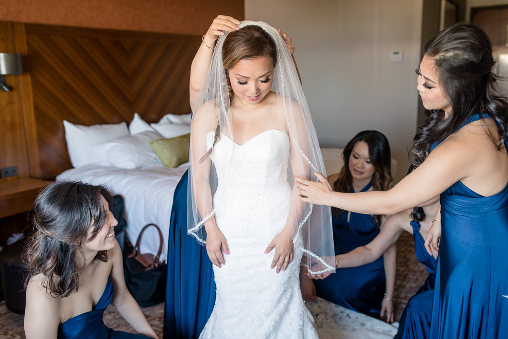 bridesmaids helping bride with her veil and dress