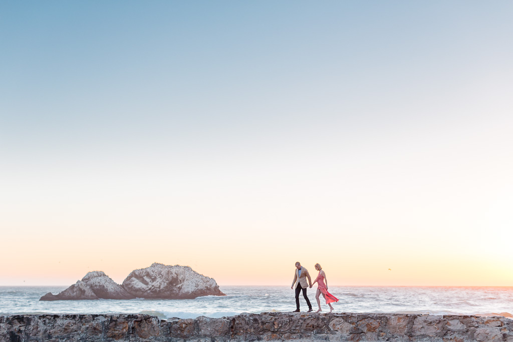 incredible engagement photo under a glowing sunset sky in a pink flowing dress blowing in the wind