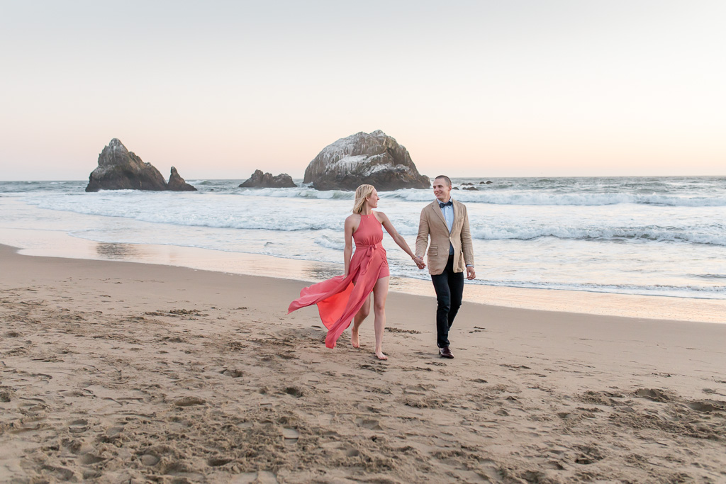walking on the beach with long pink dress billowing in the wind engagement photo