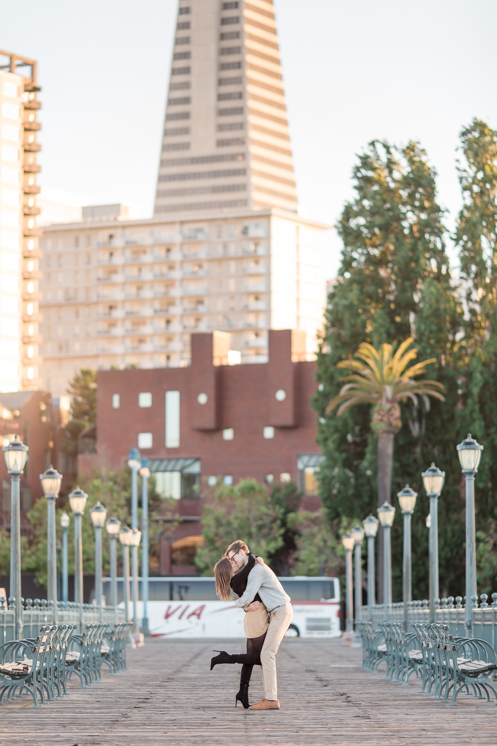 sunset kissing photo at wooden pier in front of Transamerica Pyramid building in San Francisco