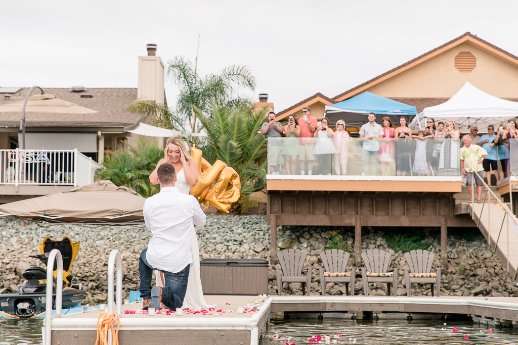 epic proposal reaction on lake dock decorated with candles and flower petals