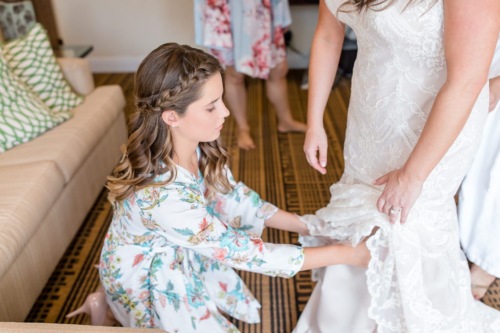 junior bridesmaid in her floral robe helping bride getting into her dress