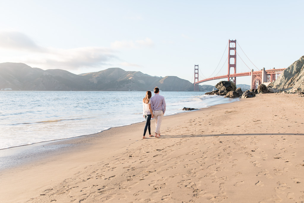 couple walking along shore towards Golden Gate Bridge