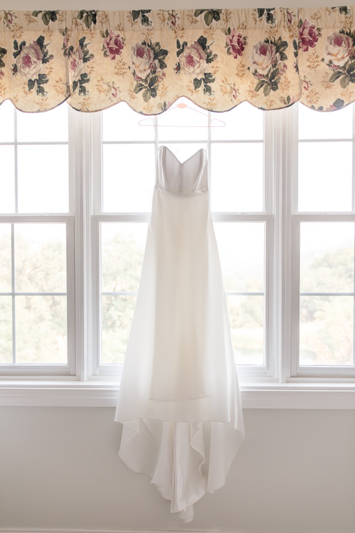 elegant and simple wedding dress hanging on the big windows