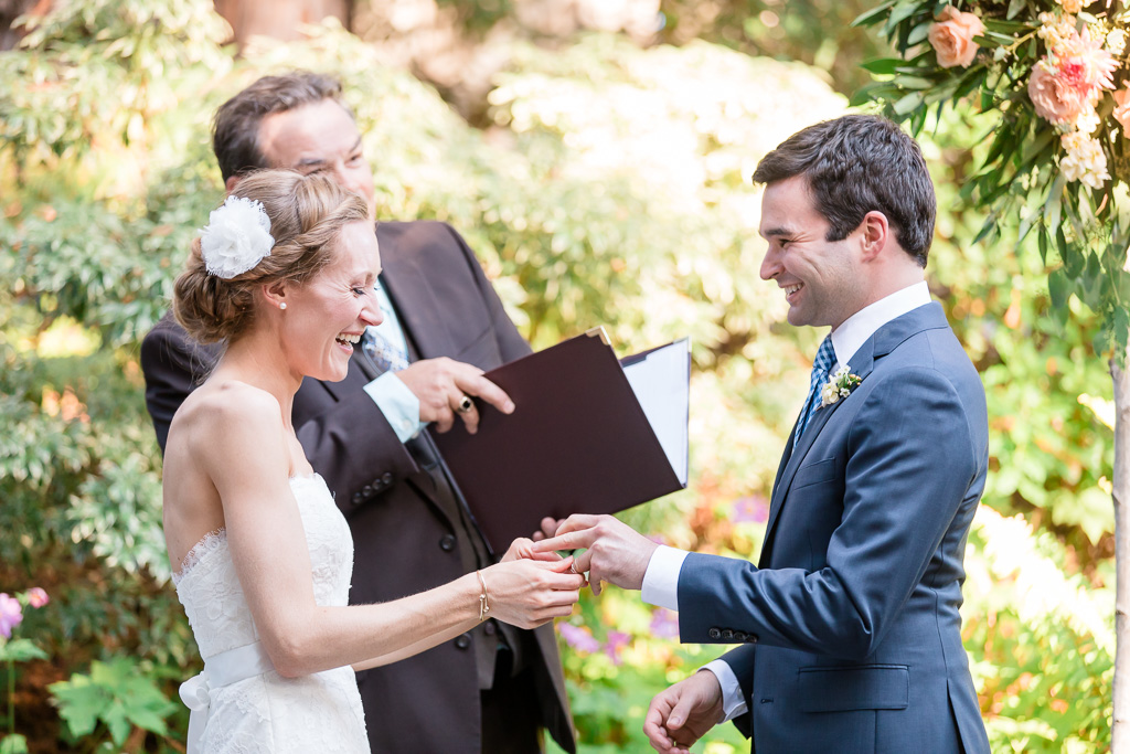 bride laughing when putting on the wedding band for groom