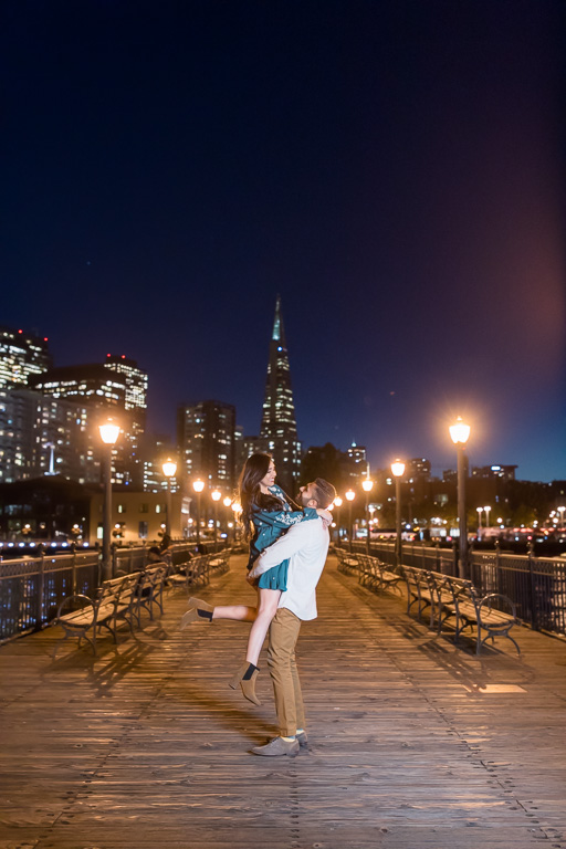 wooden pier night engagement photo at the Embarcadero with city skyline lights