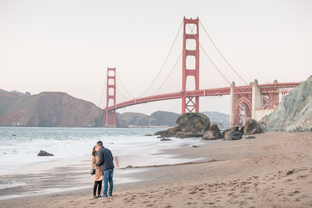 boyfriend and girlfriend kissing on beach at the Golden Gate Bridge