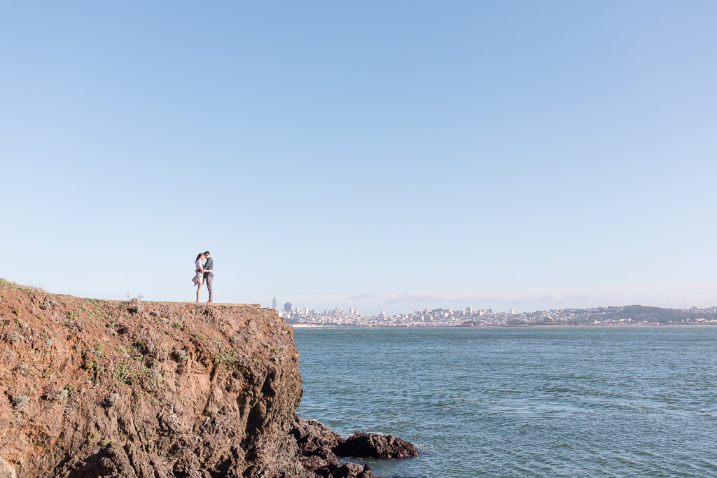 portrait of engaged couple on tall cliff with San Francisco city skyline background