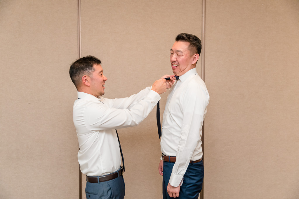 fun photo of groomsman helping groom with his tie