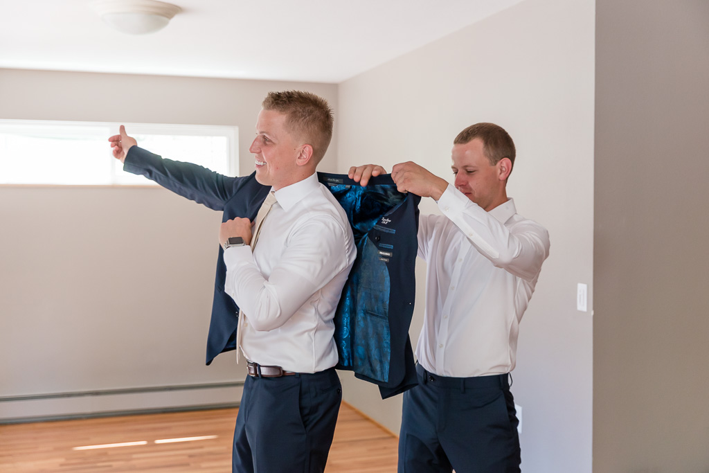 groom putting on his jacket with the help of his brother