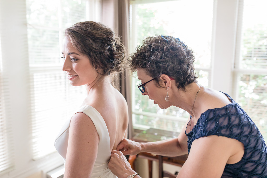 bride having her dress zipped up by mother