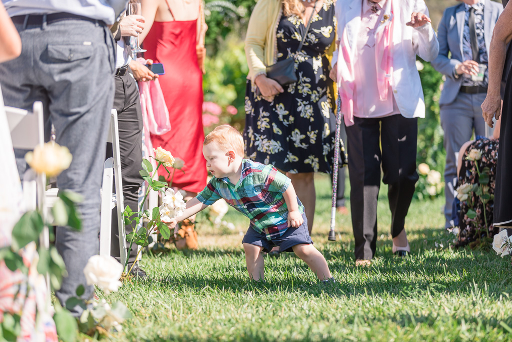 cute baby boy playing with the flowers on the ceremony aisle
