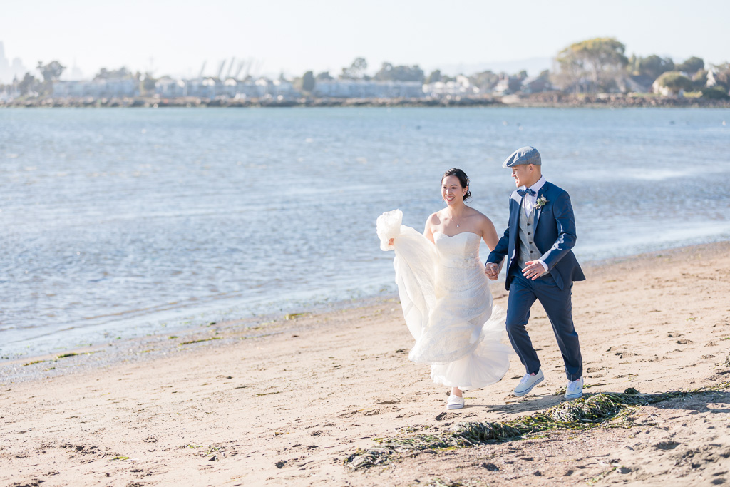 bride and groom walking along the beach with Alameda in the background
