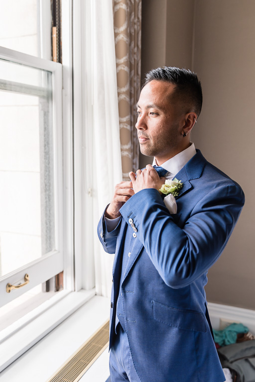 groom by hotel window adjusting tie