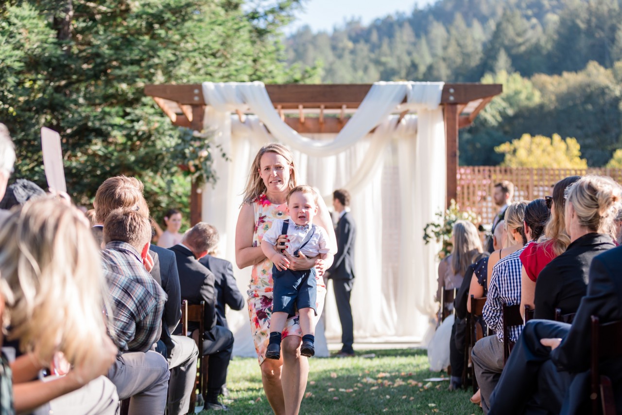 funny photo of a mom running away with a crying baby just before couple exchanges first kiss