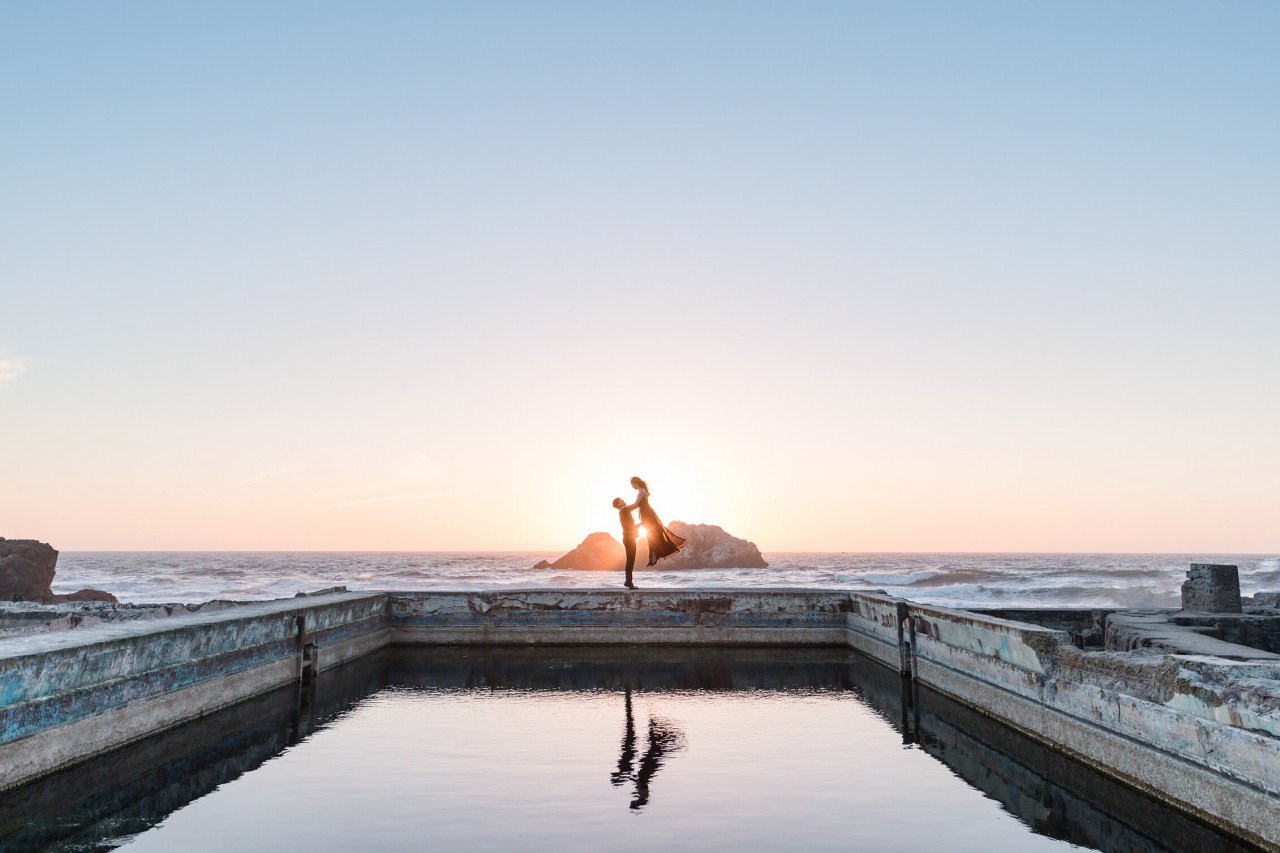 colorful sunset Sutro Baths photo with groom lifting bride up into the sky
