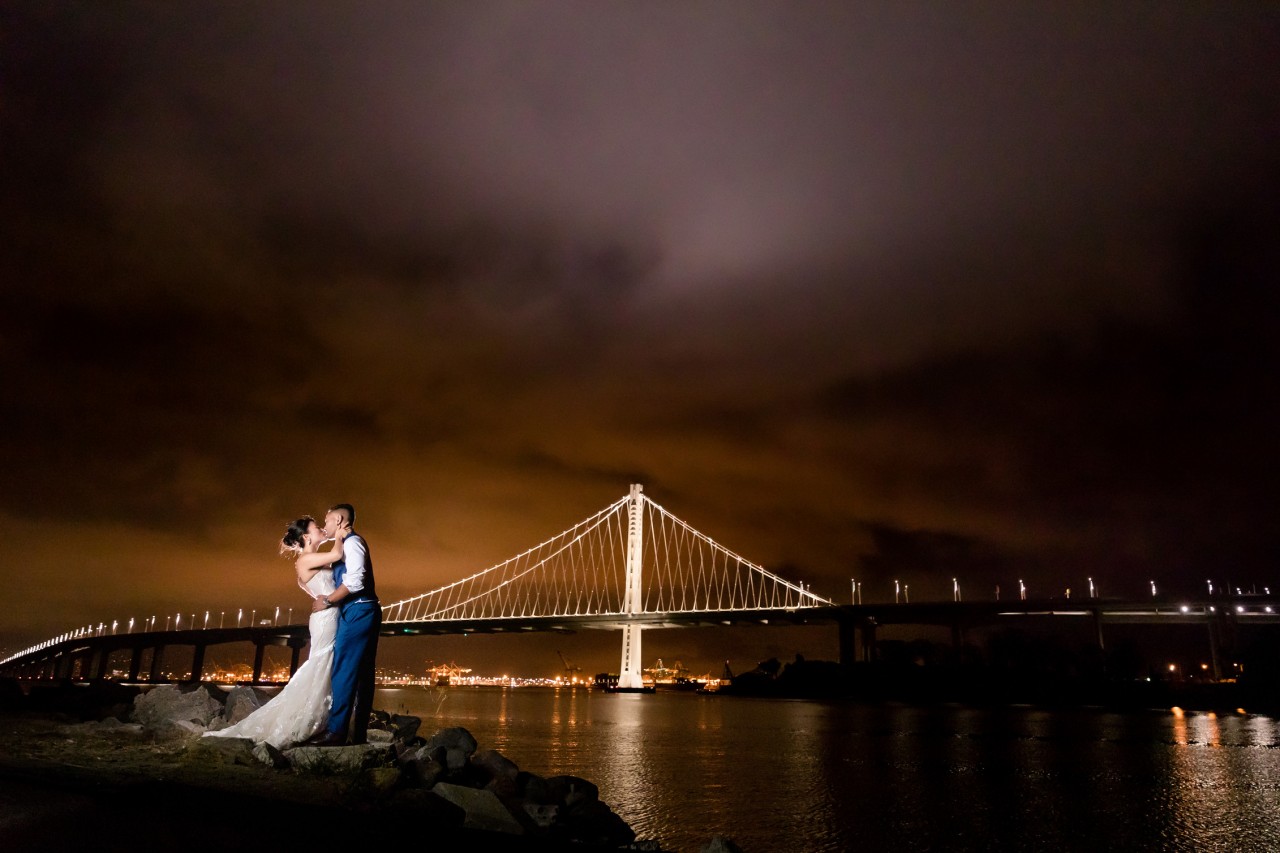 amazing wedding photo of bride and groom lit against the night sky in front of the Oakland Bay Bridge