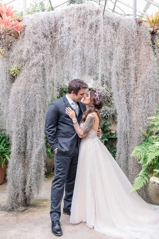 bride and groom almost kissing in front of a moss arch