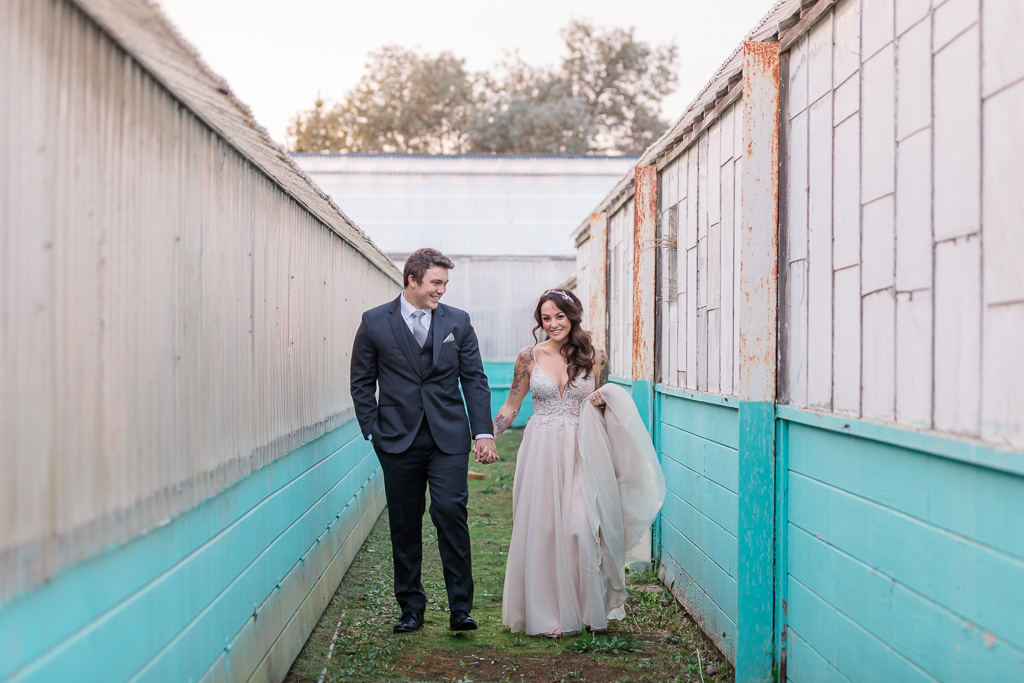 portrait of bride and groom walking between rustic buildings