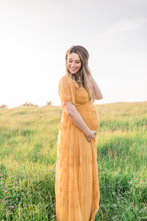 a very happy mommy-to-be standing an a green grassy field in Palo Alto