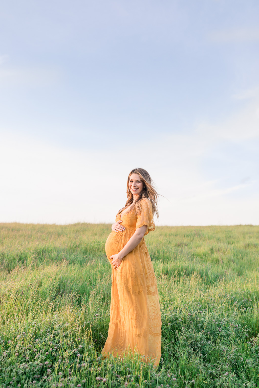 blissful maternity photo with grassy green rolling hills and blue sky