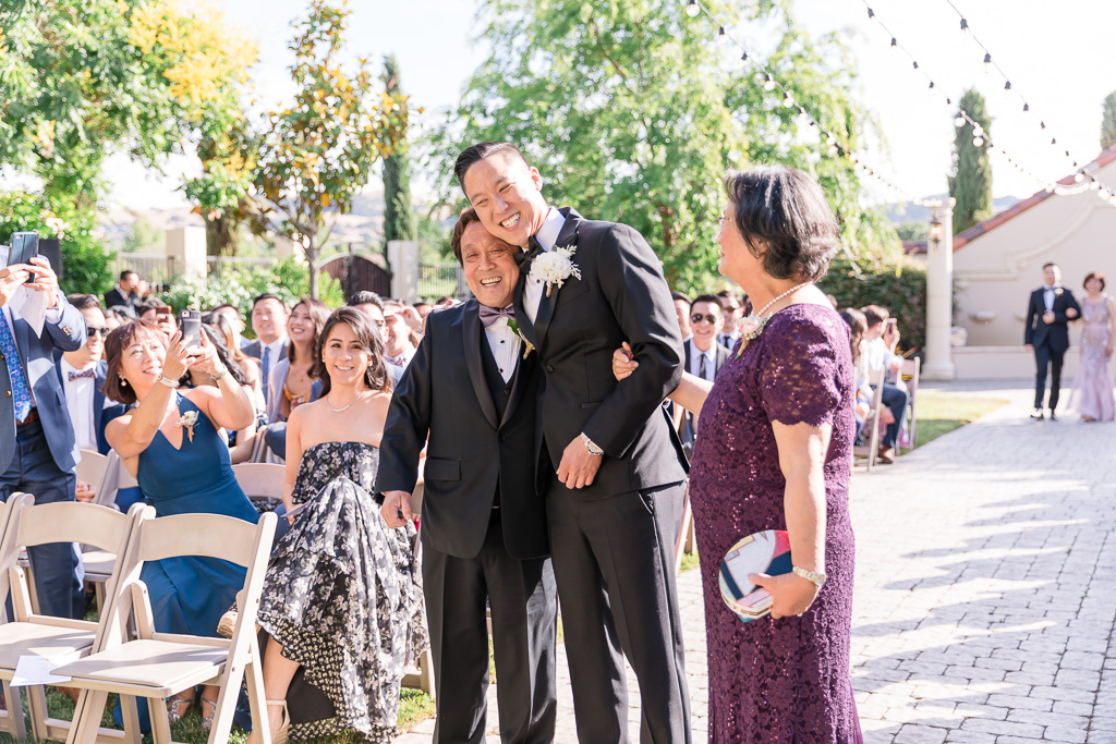 groom hugging parents at the end of the aisle
