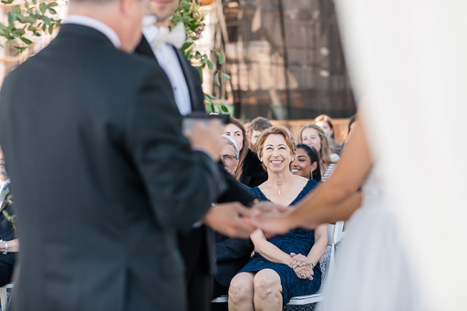 groom's mother smiling at the couple during vow exchange