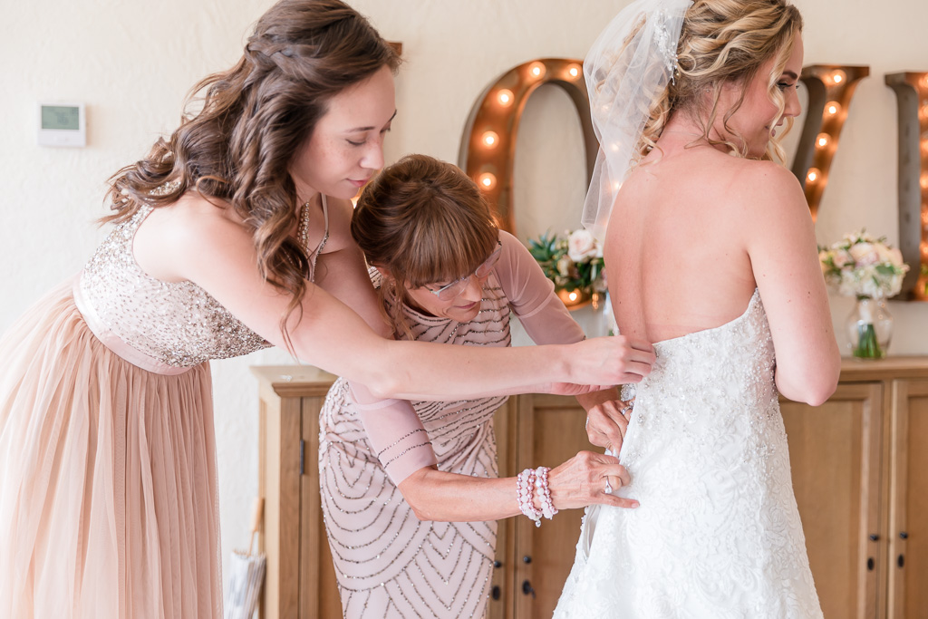 girls helping the bride to button up her gown