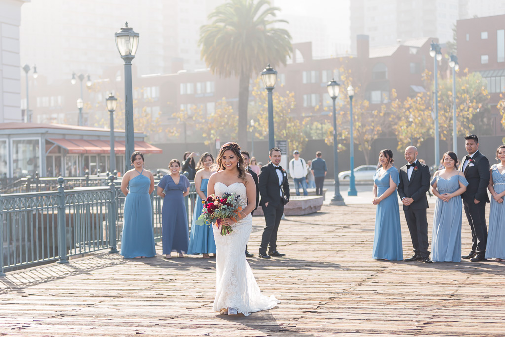 bride walking towards her groom from behind with bridal party watching