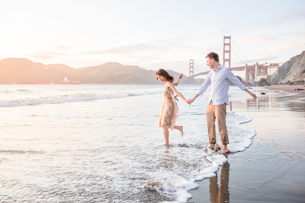 playful engaged couple kicking water on San Francisco beach