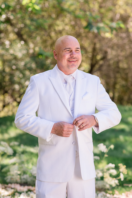 groom in a white suit buttoning jacket