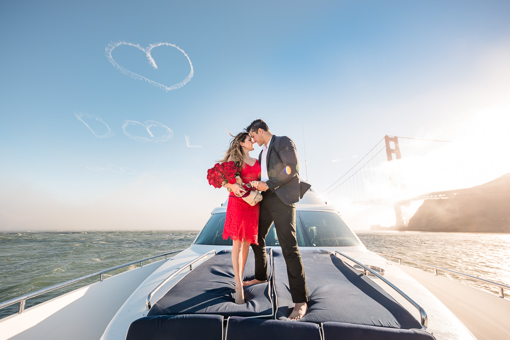 engagement photo on a yacht with heart skywriting over the Golden Gate Bridge