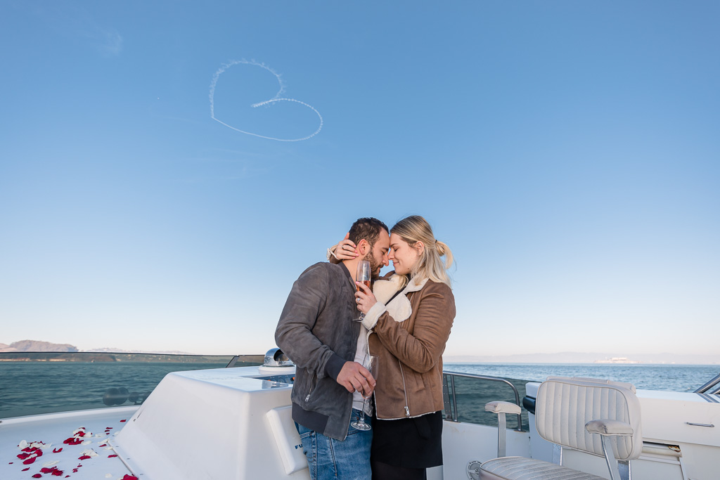 couple on a yacht under a huge heart drawn in the sky by airplane pilot
