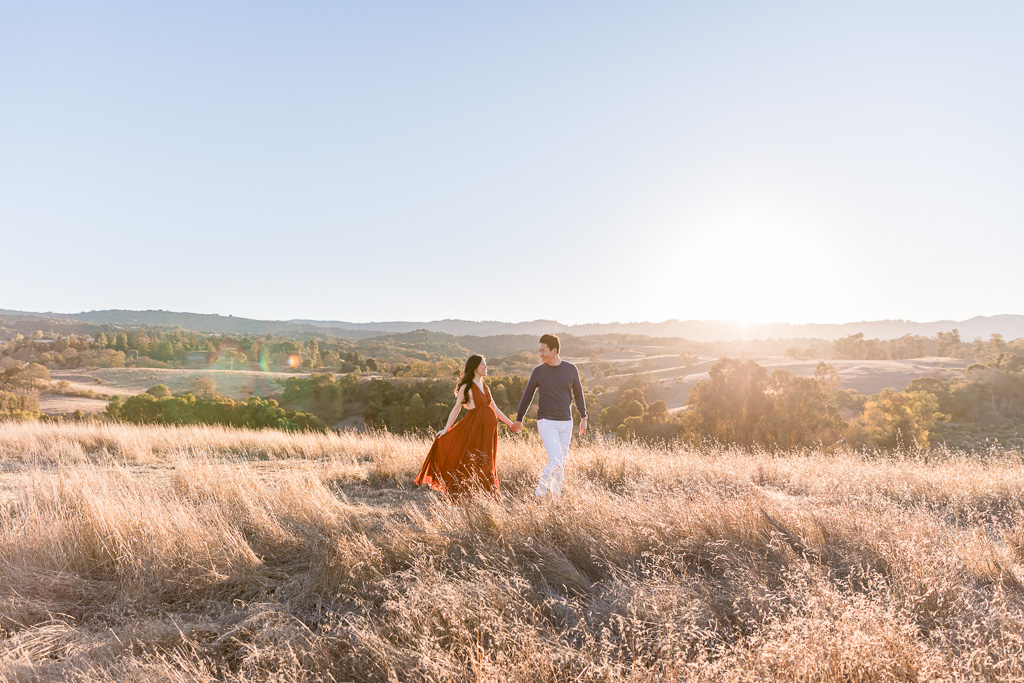 whimsical romantic maternity photo with sun flare in grassy hills