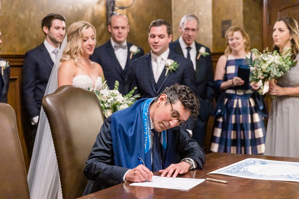 rabbi signing marriage document while bride and groom look on