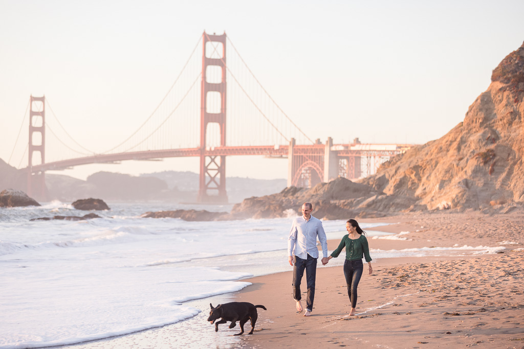 couple walking their dog on the beach in front of the Golden Gate Bridge