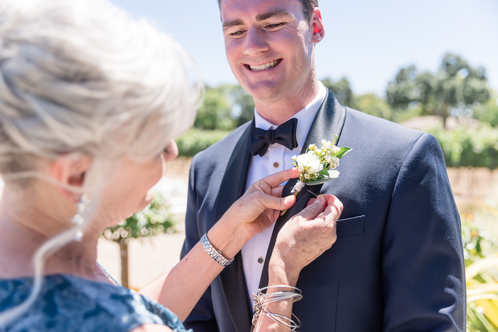 groom getting boutonniere pinned onto tux