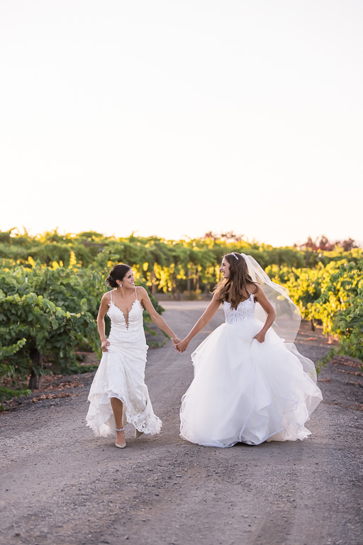 brides holding hands and skipping playfully at sunset