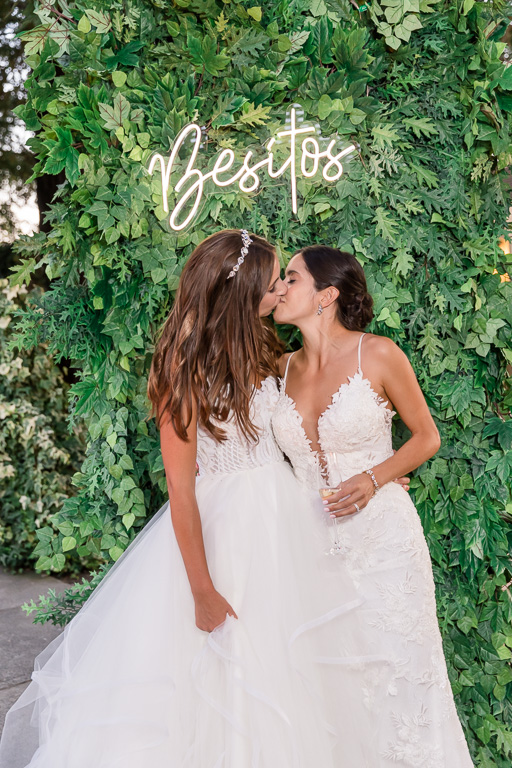 brides giving each other little kisses under a neon 