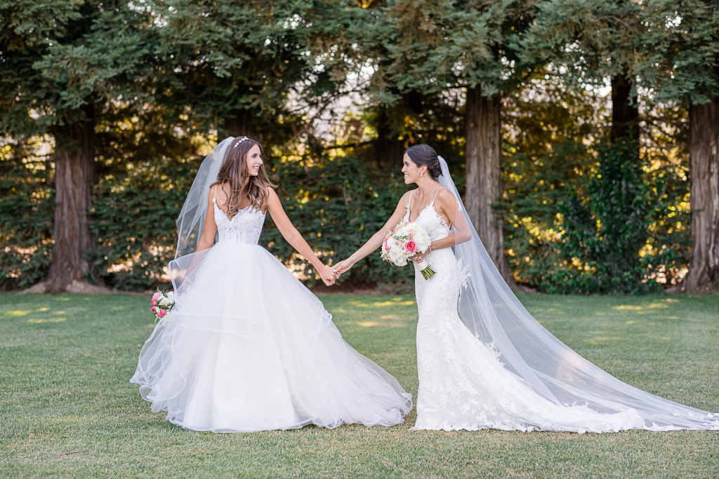 two brides walking in front of a row of trees
