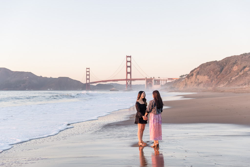 couple holding hands on the beach in front of the Golden Gate Bridge