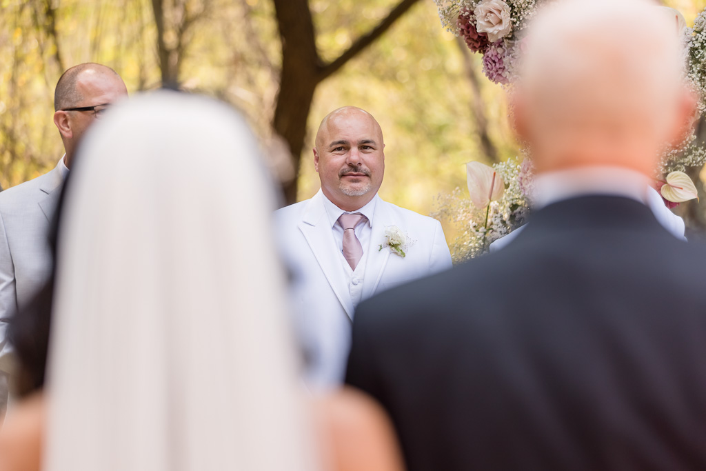 groom watches his bride walking towards him