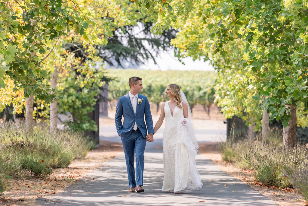 wedding photo of bride and groom walking on a road under trees in Sebastopol