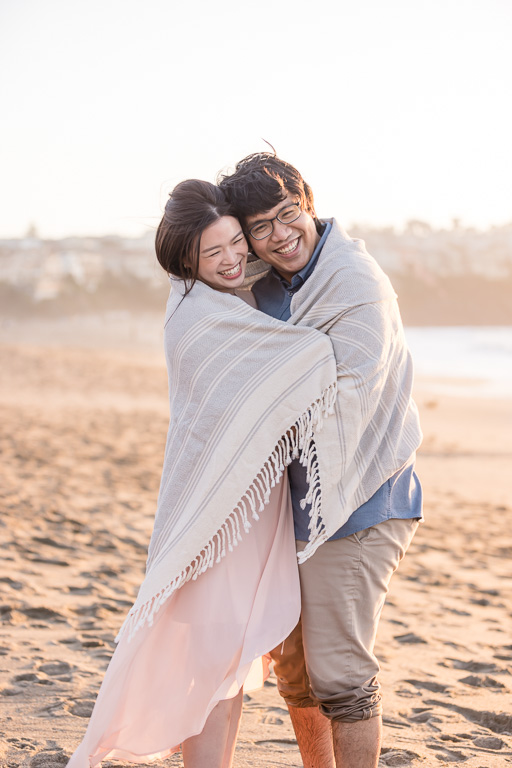 warm romantic beach engagement photo snuggled up in blanket