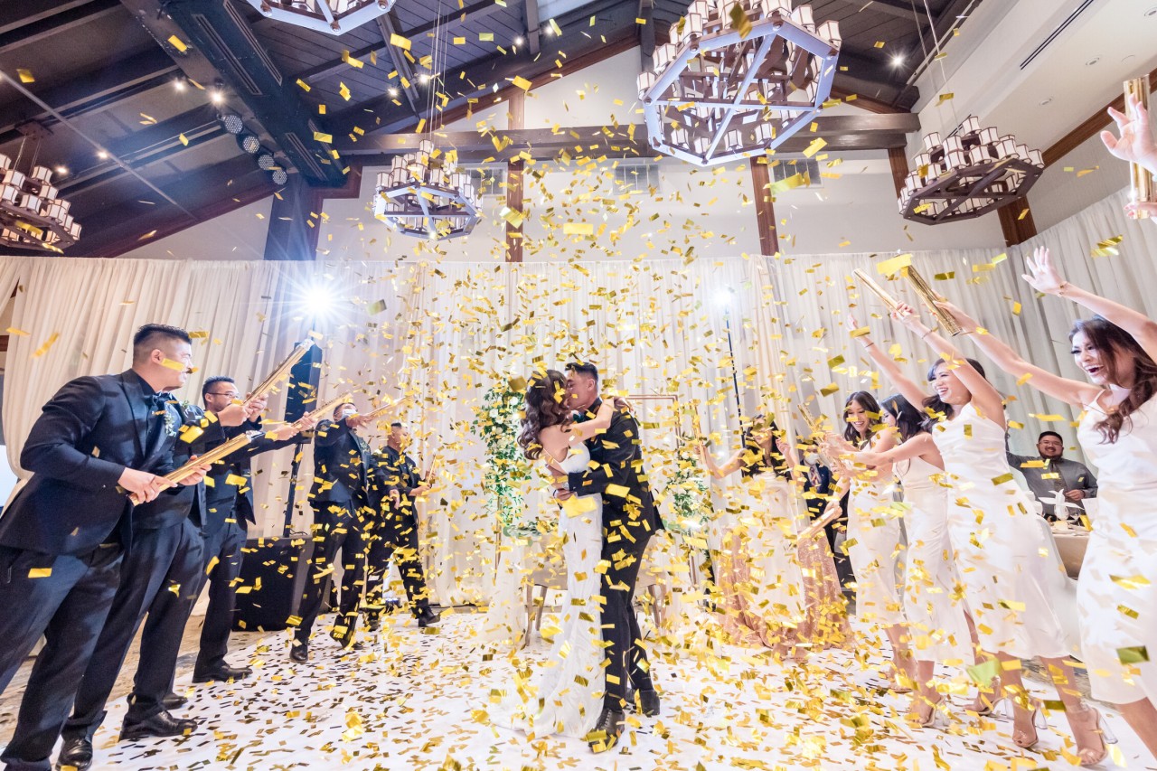 indoor wedding reception photo with golden confetti poppers flying through the air in front of bride and groom
