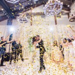 indoor wedding reception photo with golden confetti poppers flying through the air in front of bride and groom