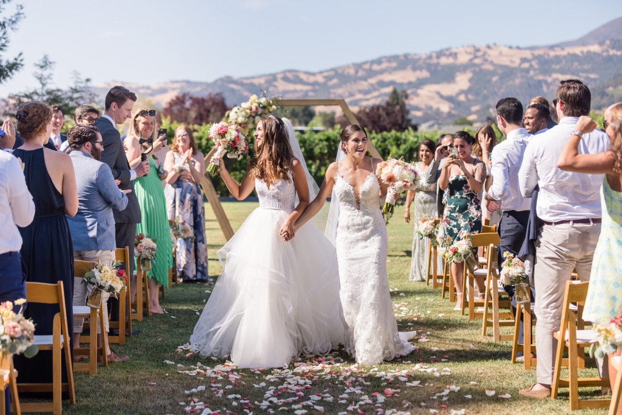 two brides cheerfully walking down the aisle after getting married