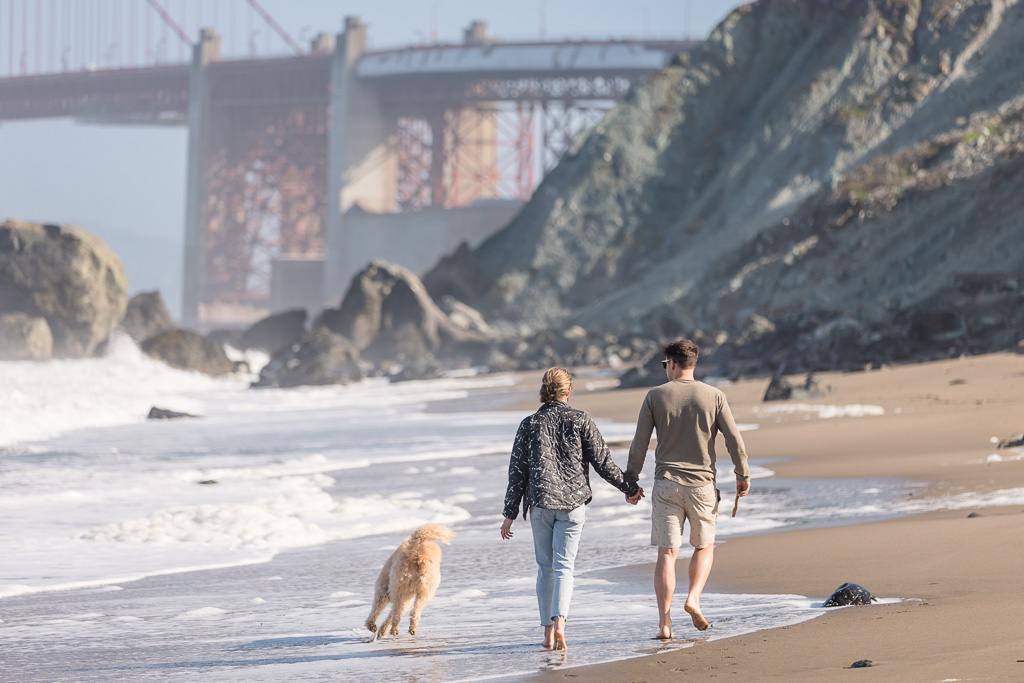couple with dog walking on the beach near the Golden Gate Bridge