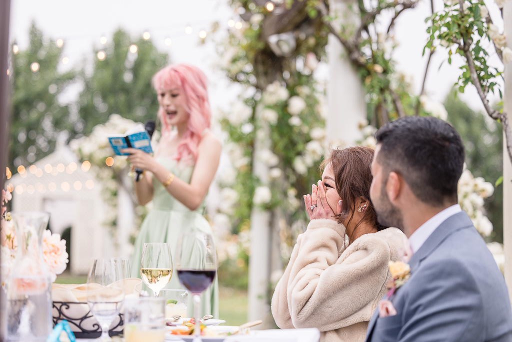 bride covering her face in embarassment while sister gives wedding toast