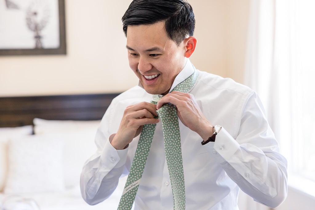 groom putting on sage colored dotted tie